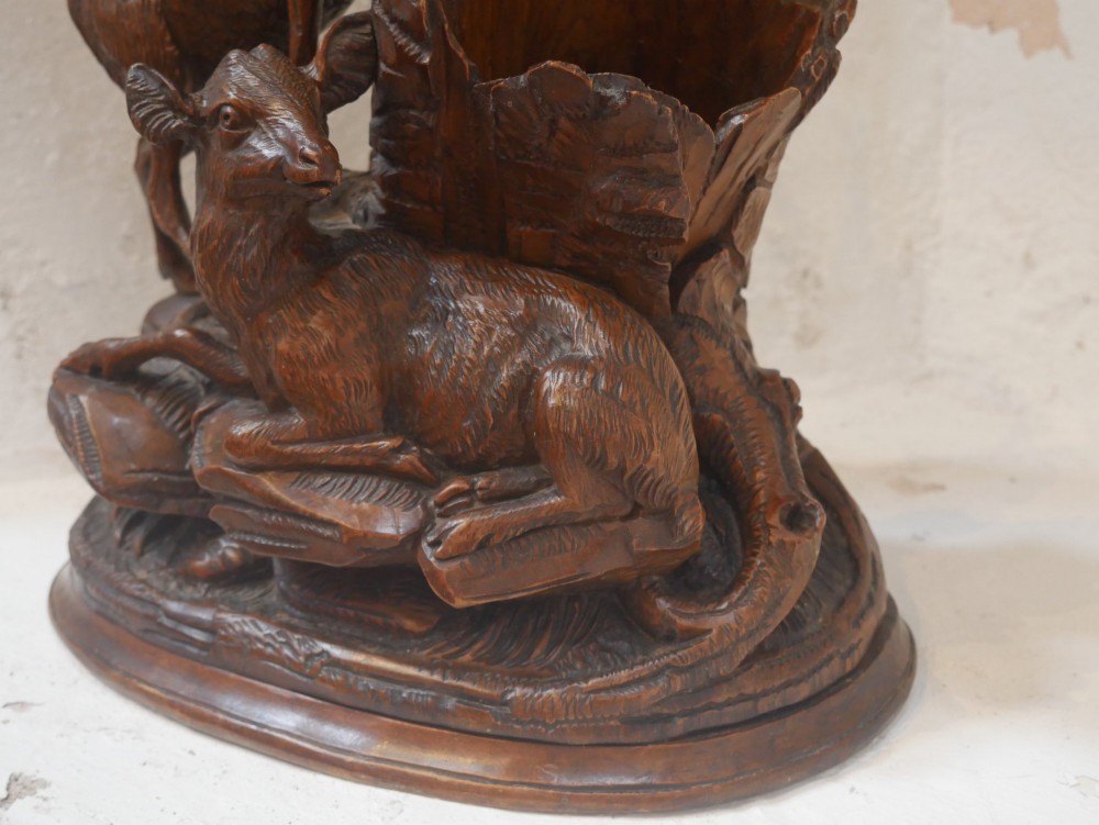 A hand-carved dark wood Black Forest sculpture depicting two mountain goats positioned beside a hollow tree stump on an oval base. View II