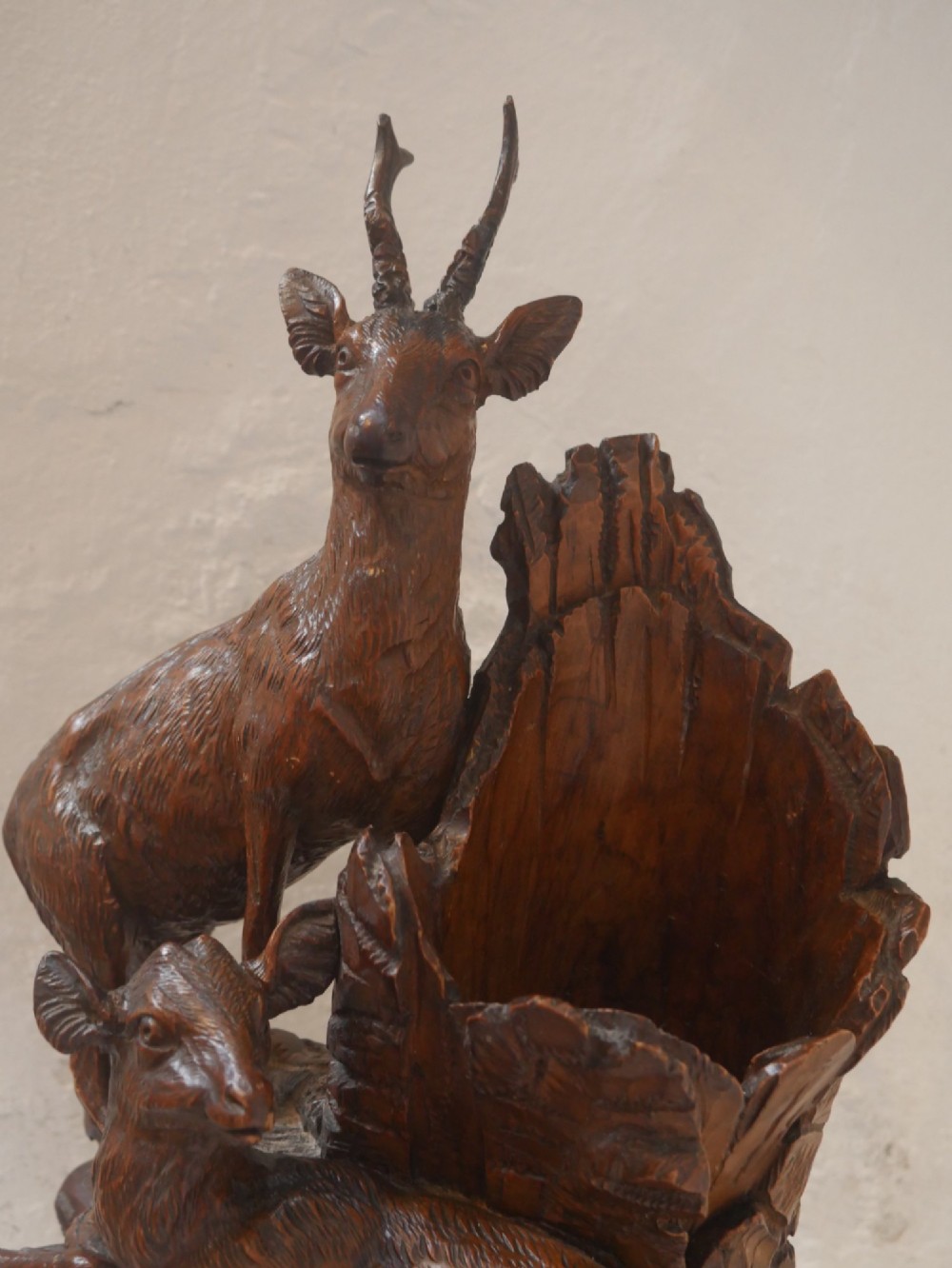 A hand-carved dark wood Black Forest sculpture depicting two mountain goats positioned beside a hollow tree stump on an oval base. View III