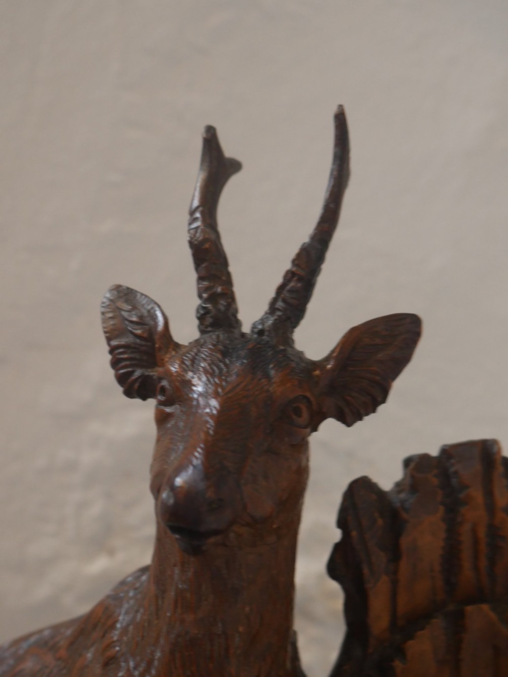 A hand-carved dark wood Black Forest sculpture depicting two mountain goats positioned beside a hollow tree stump on an oval base. View IV