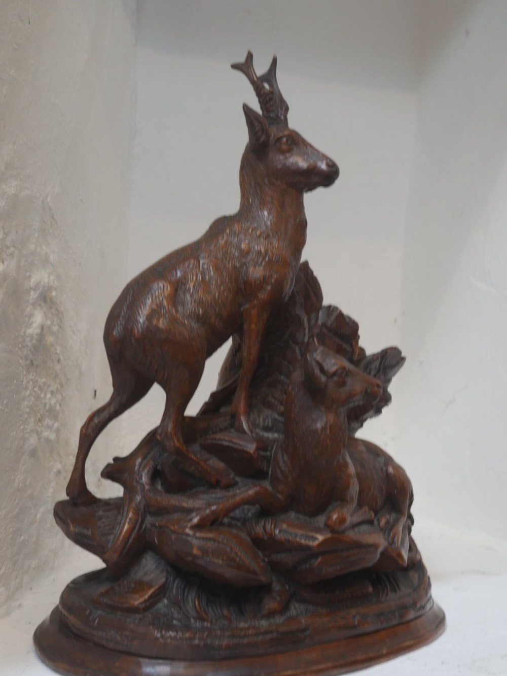 A hand-carved dark wood Black Forest sculpture depicting two mountain goats positioned beside a hollow tree stump on an oval base. View V
