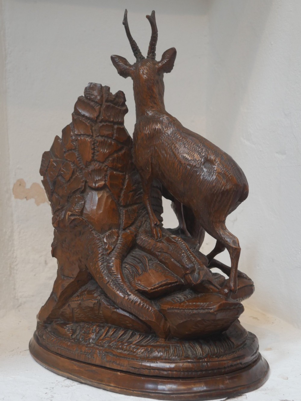 A hand-carved dark wood Black Forest sculpture depicting two mountain goats positioned beside a hollow tree stump on an oval base. View VII