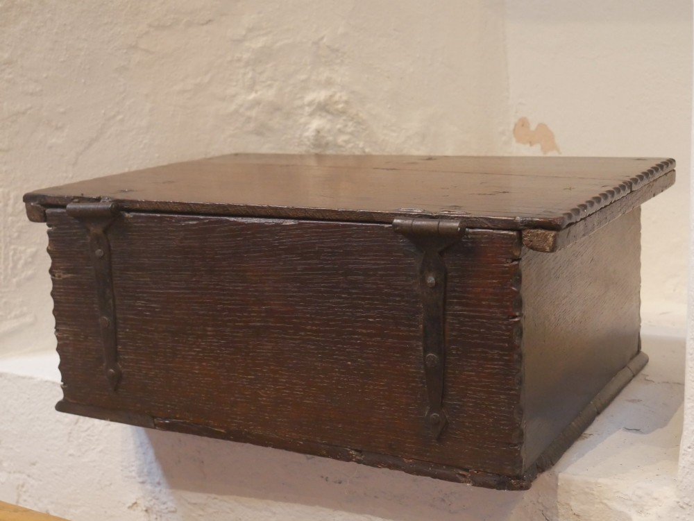 A dark carved oak box with hand-carved botanical motifs on the front panel and a central iron lockplate. View V