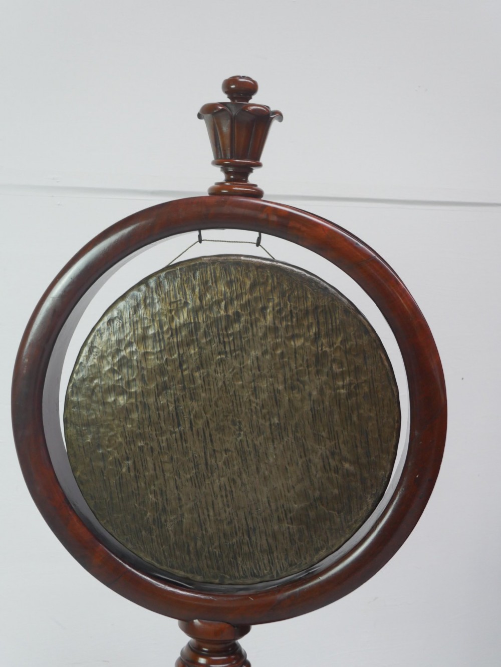 A carved mahogany standing dinner gong featuring a circular frame with a suspended beaten brass gong disc on a turned pedestal. View II