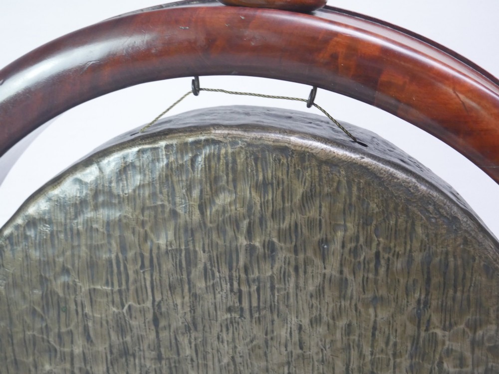 A carved mahogany standing dinner gong featuring a circular frame with a suspended beaten brass gong disc on a turned pedestal. View VII