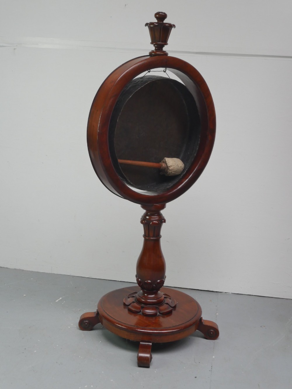 A carved mahogany standing dinner gong featuring a circular frame with a suspended beaten brass gong disc on a turned pedestal. View IX