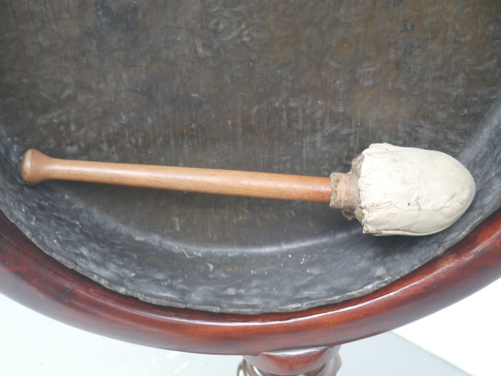A carved mahogany standing dinner gong featuring a circular frame with a suspended beaten brass gong disc on a turned pedestal. View X