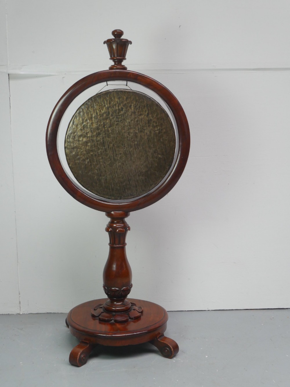 A carved mahogany standing dinner gong featuring a circular frame with a suspended beaten brass gong disc on a turned pedestal. View XII