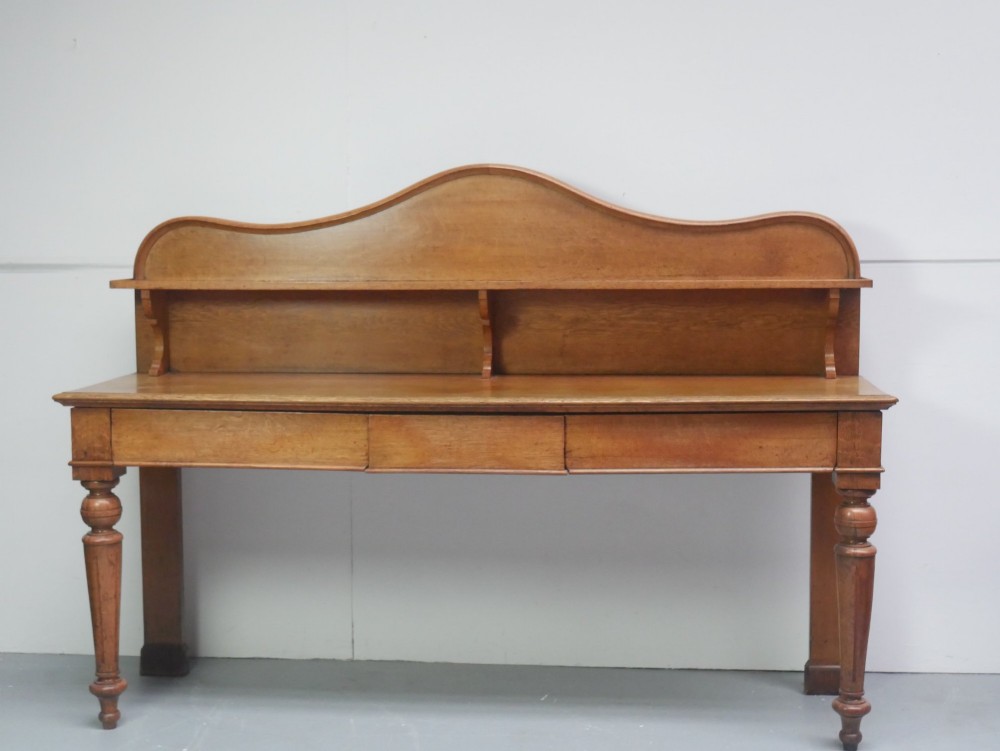 A large Victorian oak serving table featuring a raised back gallery shelf, frieze drawers, and turned front legs. View II