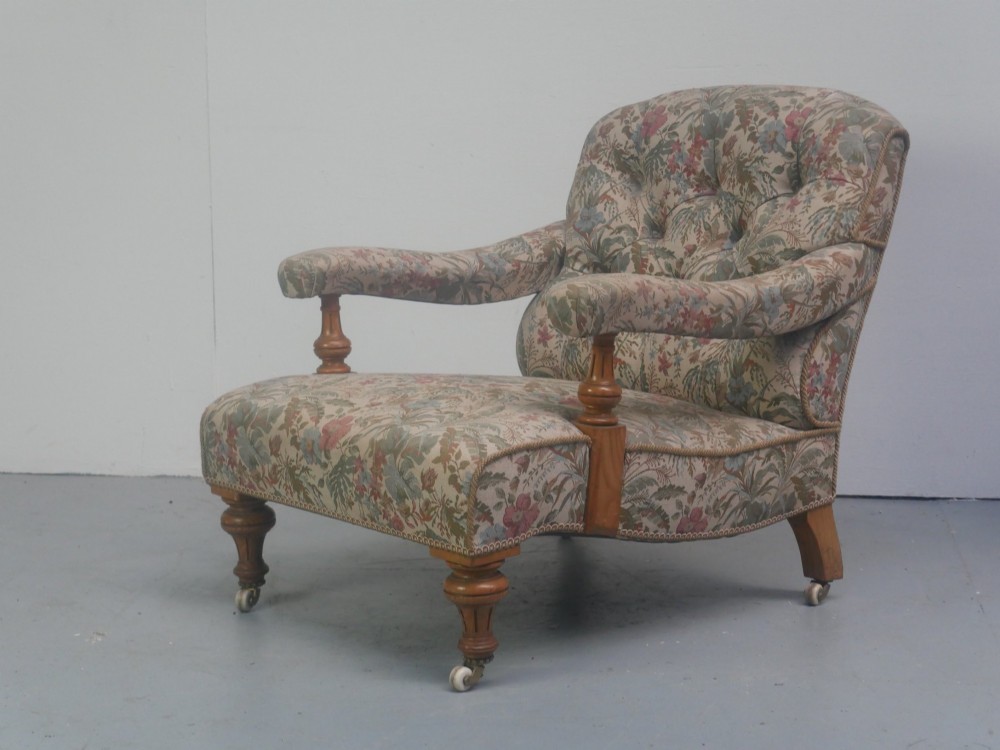 A 19th-century Howard style armchair with button-tufted floral tapestry upholstery, low padded arms, turned timber legs, and ceramic castors.