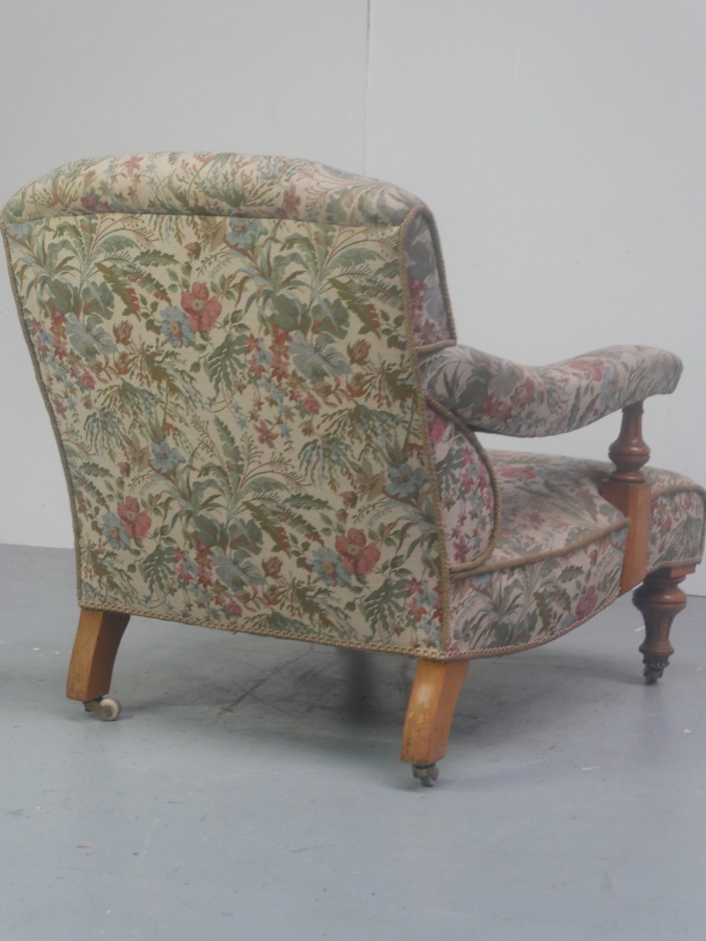 A 19th-century Howard style armchair with button-tufted floral tapestry upholstery, low padded arms, turned timber legs, and ceramic castors. View IV