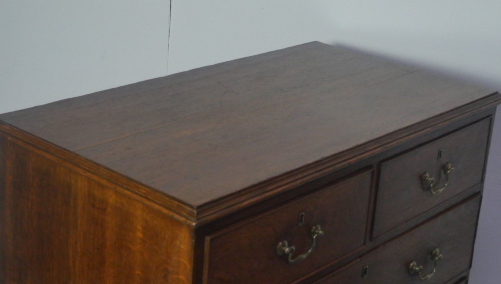 A Georgian oak chest of drawers featuring two short drawers over three long graduated drawers with brass swan-neck handles and bracket feet. View II