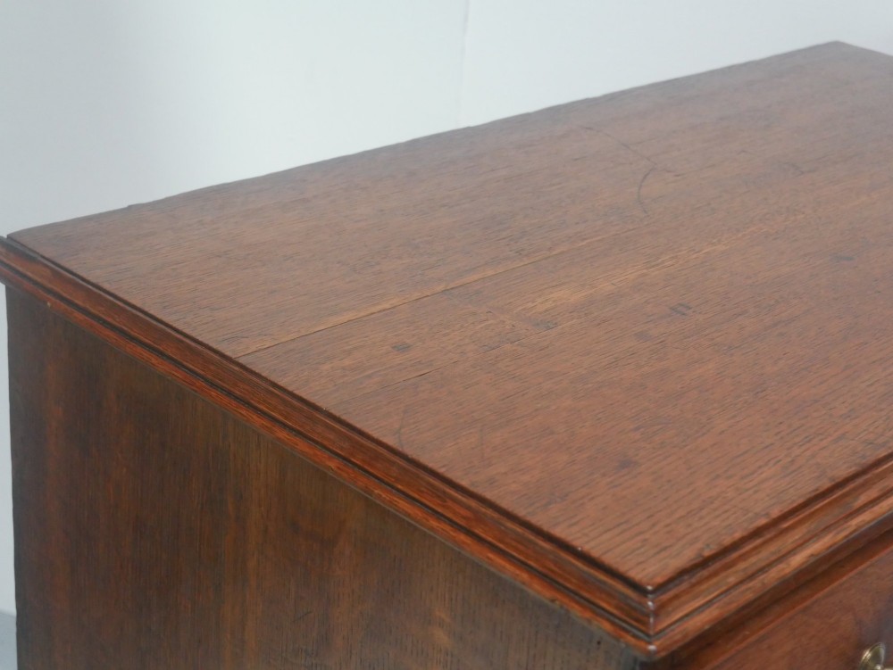 A Georgian oak chest of drawers featuring two short drawers over three long graduated drawers with brass swan-neck handles and bracket feet. View IV