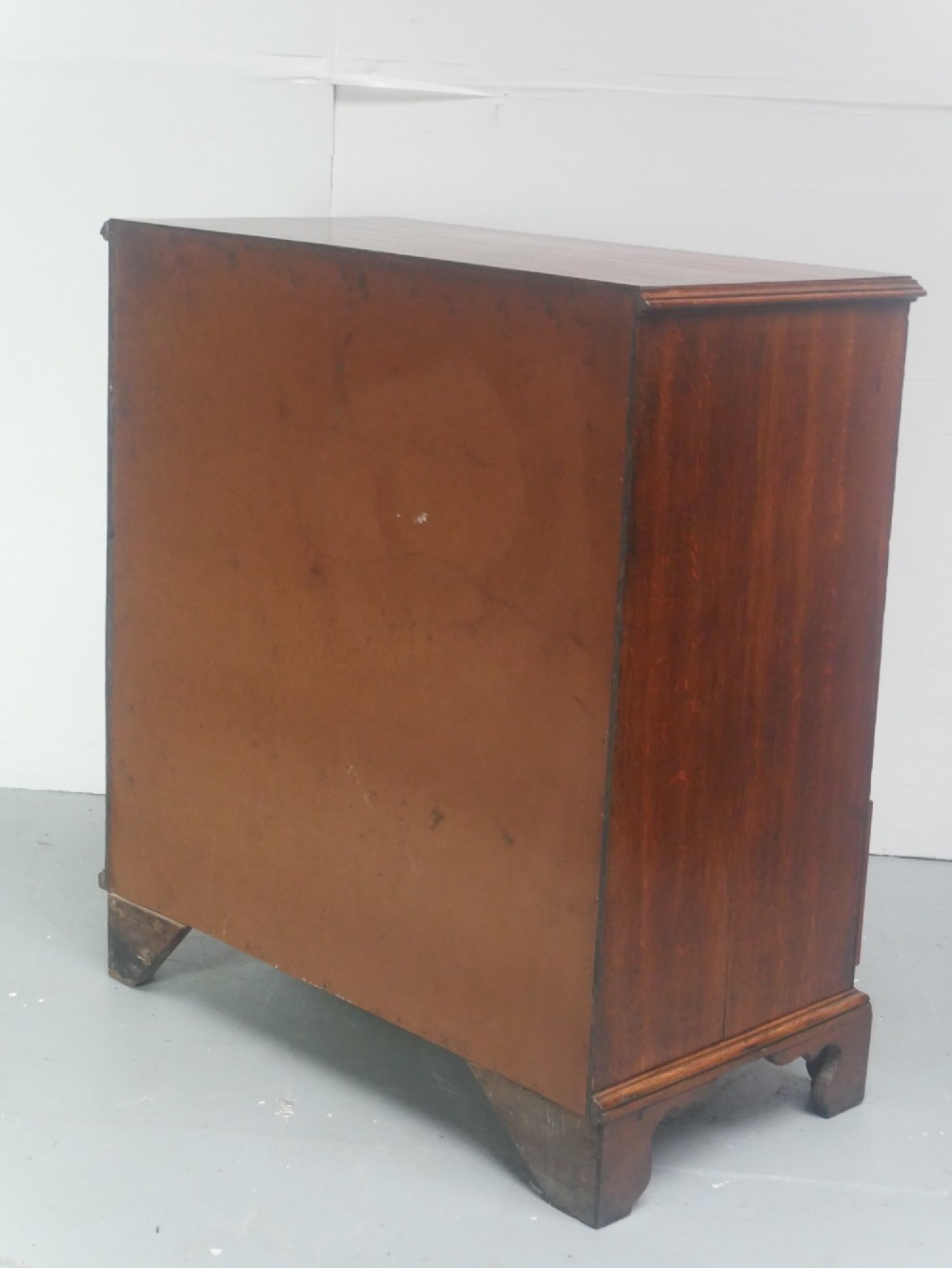 A Georgian oak chest of drawers featuring two short drawers over three long graduated drawers with brass swan-neck handles and bracket feet. View V