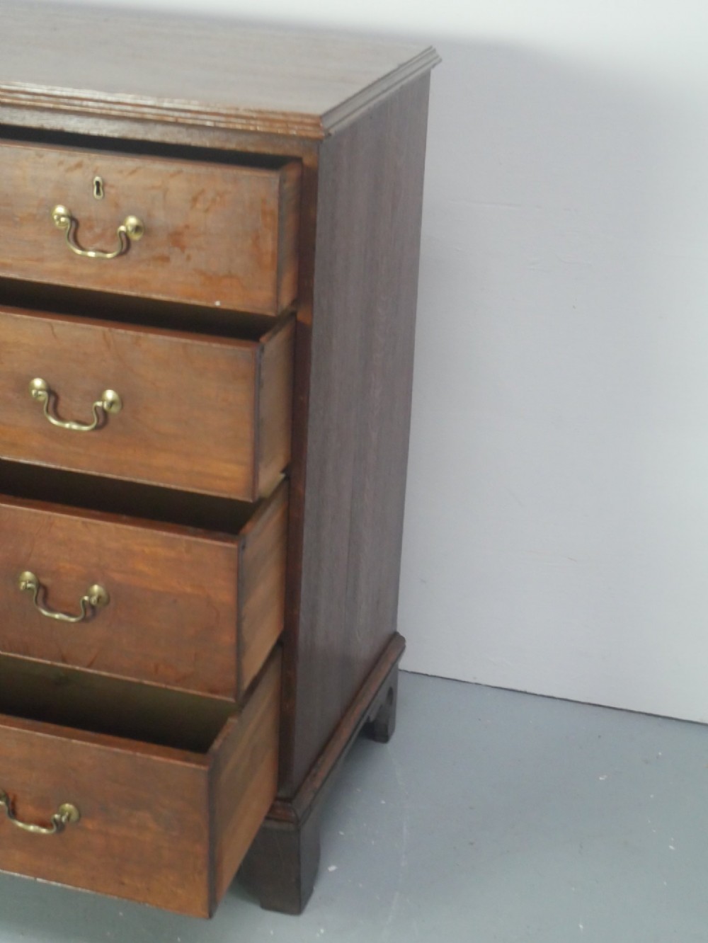 A Georgian oak chest of drawers featuring two short drawers over three long graduated drawers with brass swan-neck handles and bracket feet. View IX