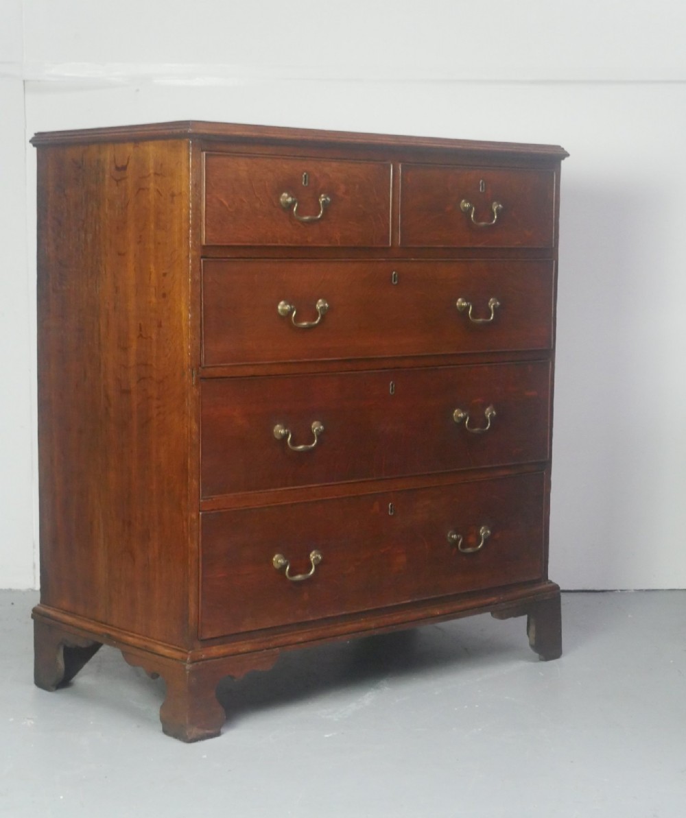 A Georgian oak chest of drawers featuring two short drawers over three long graduated drawers with brass swan-neck handles and bracket feet. View X