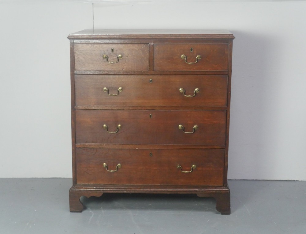 A Georgian oak chest of drawers featuring two short drawers over three long graduated drawers with brass swan-neck handles and bracket feet. View XII