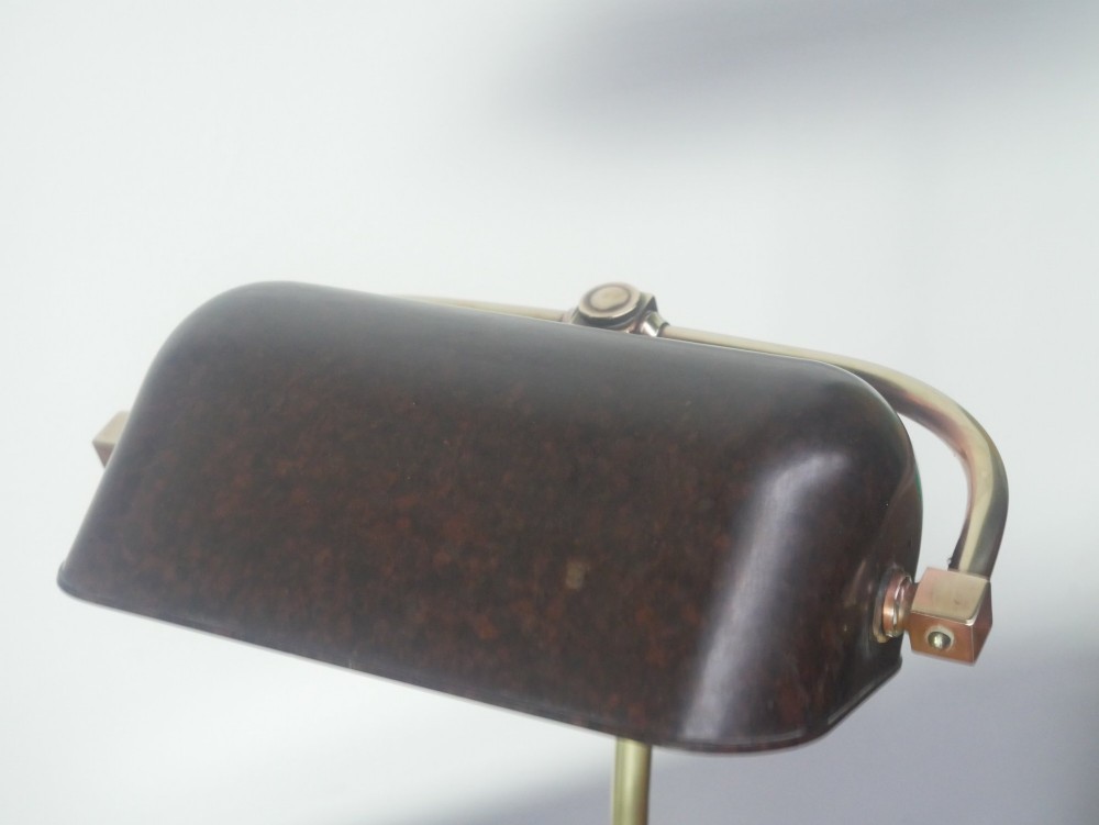 A vintage brass bankers desk lamp featuring a weighted round base, curved stem, and adjustable dark metal shade. View V