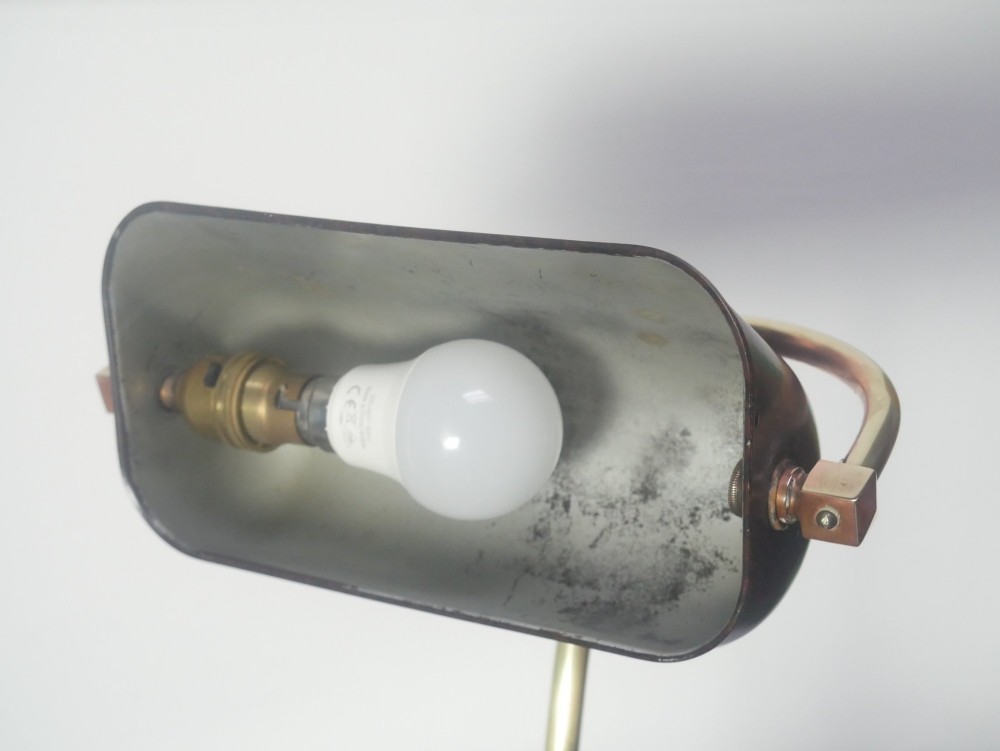 A vintage brass bankers desk lamp featuring a weighted round base, curved stem, and adjustable dark metal shade. View VII