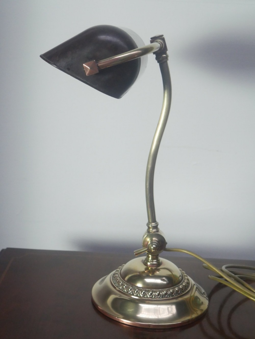 A vintage brass bankers desk lamp featuring a weighted round base, curved stem, and adjustable dark metal shade. View VIII