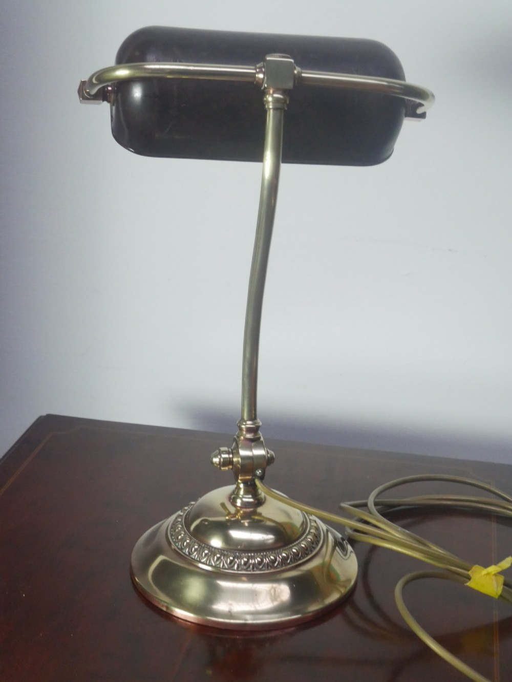 A vintage brass bankers desk lamp featuring a weighted round base, curved stem, and adjustable dark metal shade. View X