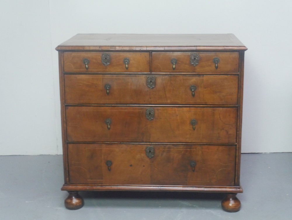 An early 18th century walnut chest of drawers featuring geometric line inlay, brass drop handles, decorative escutcheons, and turned bun feet. View II