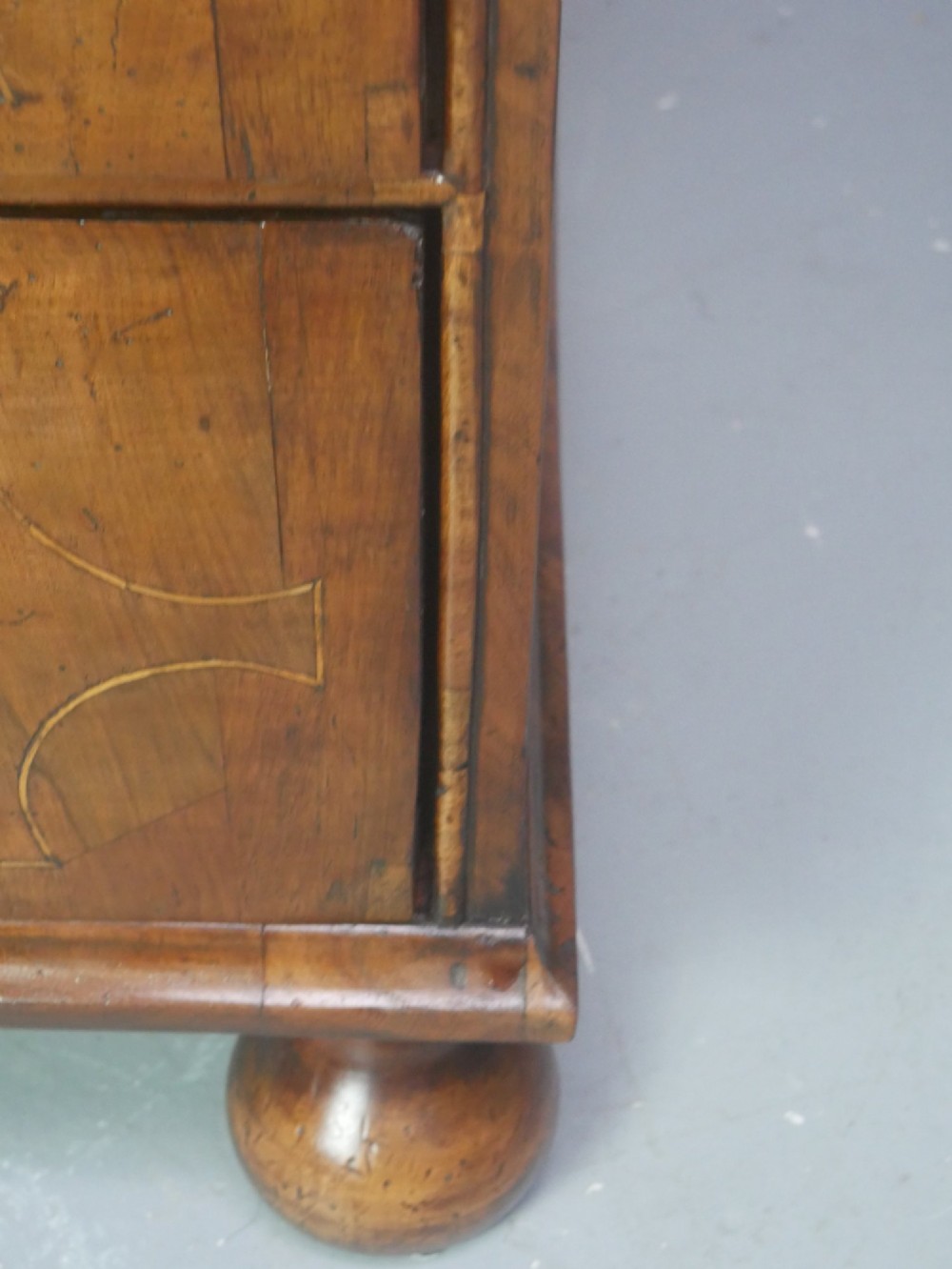 An early 18th century walnut chest of drawers featuring geometric line inlay, brass drop handles, decorative escutcheons, and turned bun feet. View III