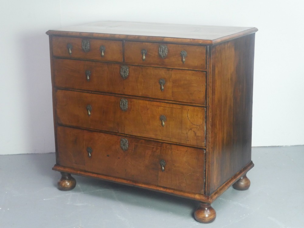 An early 18th century walnut chest of drawers featuring geometric line inlay, brass drop handles, decorative escutcheons, and turned bun feet. View IV