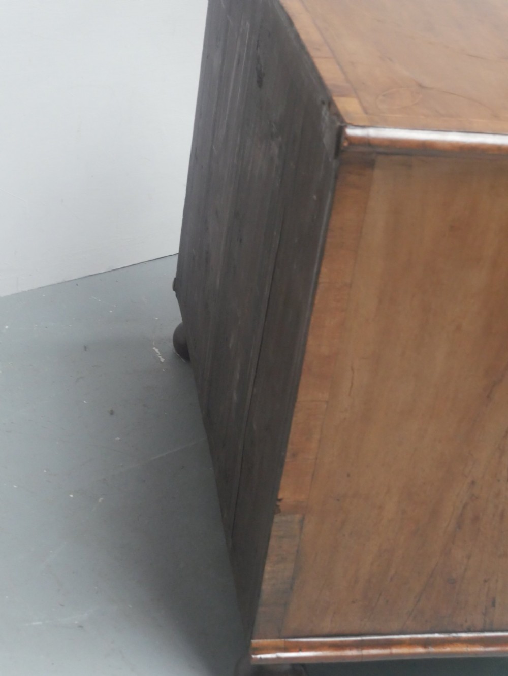 An early 18th century walnut chest of drawers featuring geometric line inlay, brass drop handles, decorative escutcheons, and turned bun feet. View VI