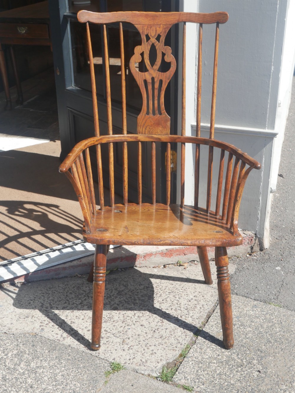 A Georgian comb back Windsor armchair featuring vertical wooden spindles, a pierced central splat, curved armrests, and turned legs.