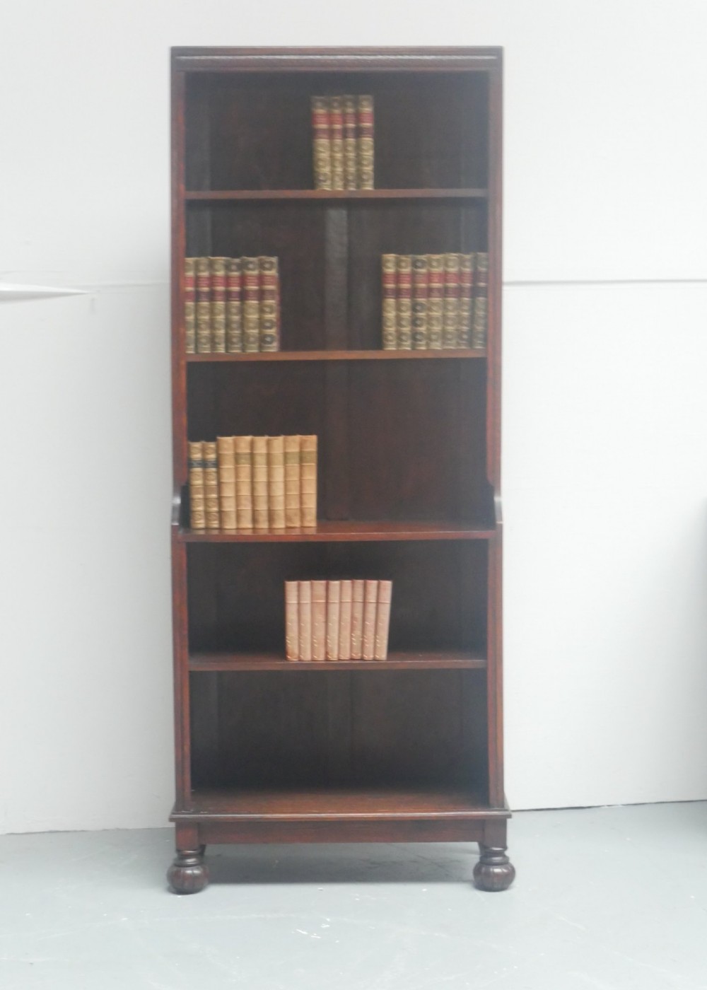 A tall, narrow 1920s dark oak open bookcase featuring five shelves and turned bun feet. View X