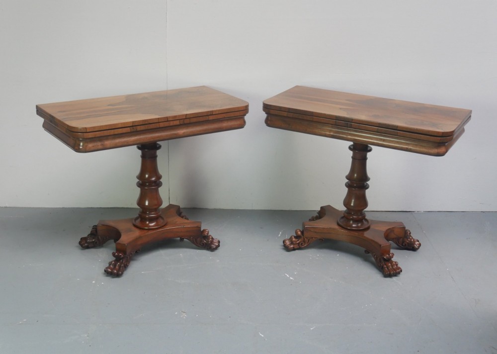 A pair of antique rosewood fold-over tea tables featuring turned pedestal columns and quadform bases with carved feet.