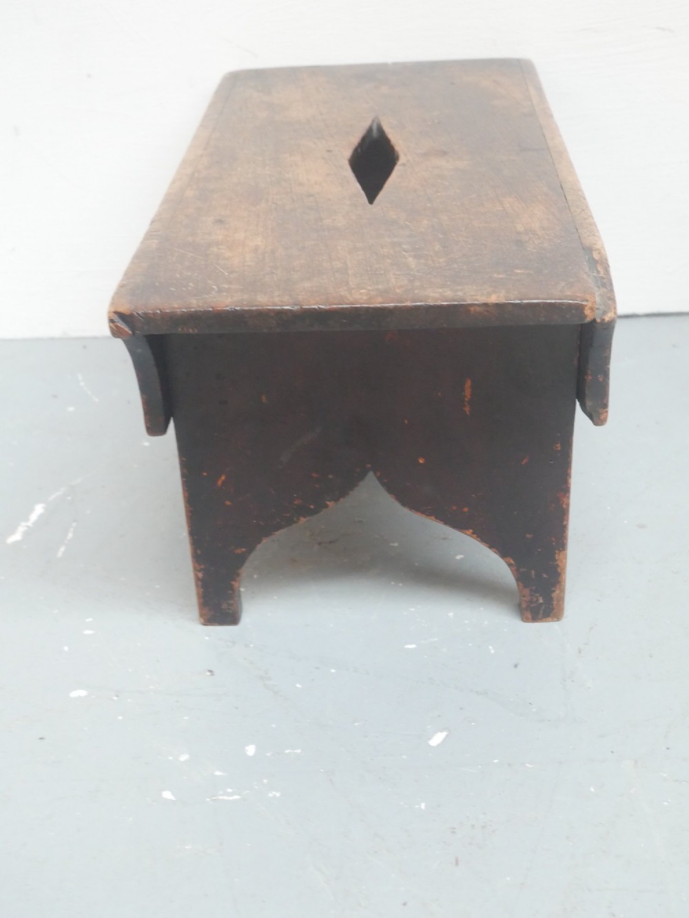 A small antique Scottish vernacular creepie stool constructed from dark patinated wood with a central handhole aperture and shaped board legs. View III