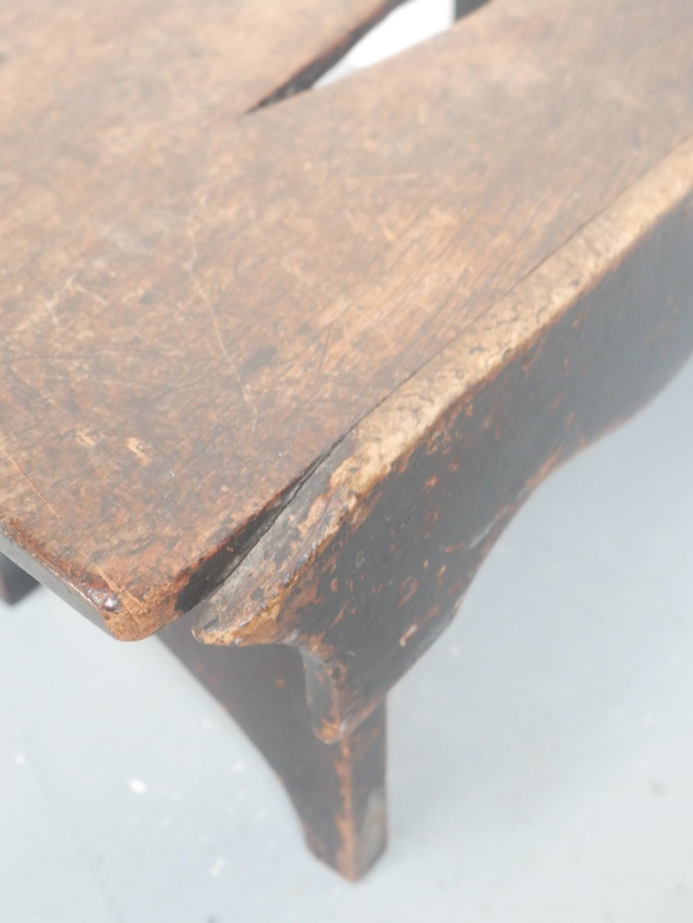 A small antique Scottish vernacular creepie stool constructed from dark patinated wood with a central handhole aperture and shaped board legs. View IV