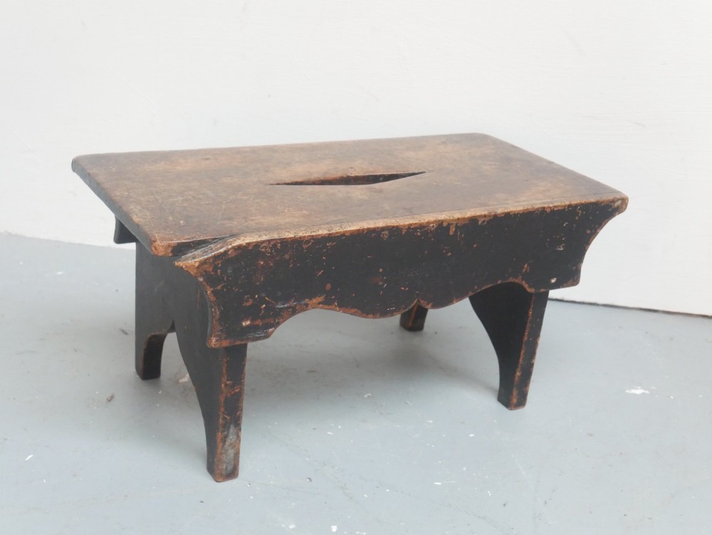 A small antique Scottish vernacular creepie stool constructed from dark patinated wood with a central handhole aperture and shaped board legs. View V