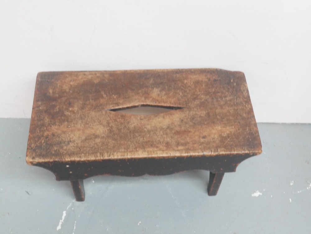 A small antique Scottish vernacular creepie stool constructed from dark patinated wood with a central handhole aperture and shaped board legs. View VII