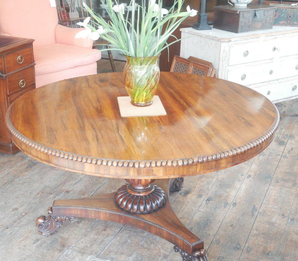 A Regency mahogany circular centre table featuring a beaded moulding edge, a carved gadrooned pedestal, and a triform base with scrolled feet.