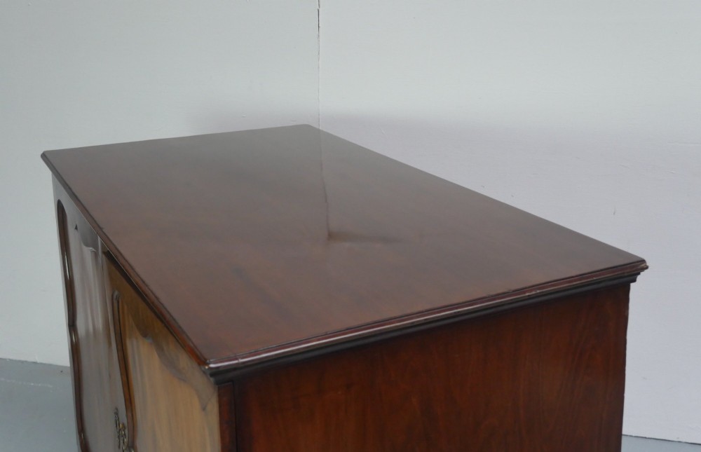 A low Georgian mahogany linen cupboard featuring two shaped panel doors, brass keyhole escutcheons, side handles, and bracket feet. View III