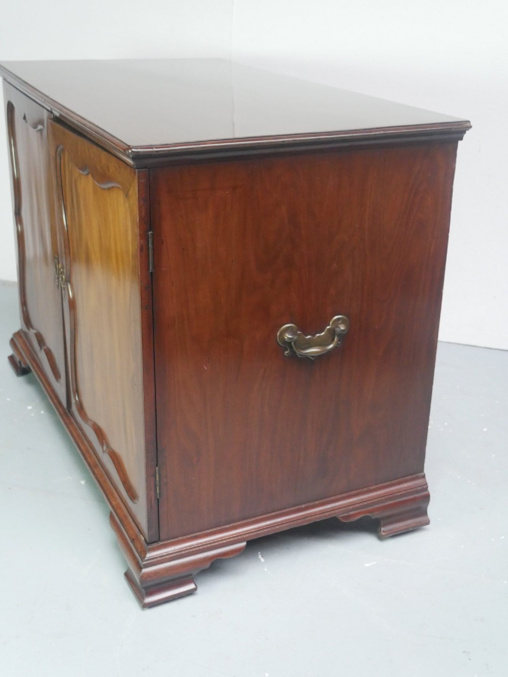A low Georgian mahogany linen cupboard featuring two shaped panel doors, brass keyhole escutcheons, side handles, and bracket feet. View IV
