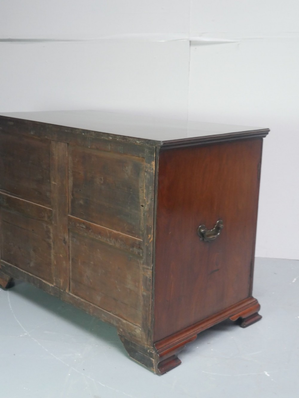 A low Georgian mahogany linen cupboard featuring two shaped panel doors, brass keyhole escutcheons, side handles, and bracket feet. View V