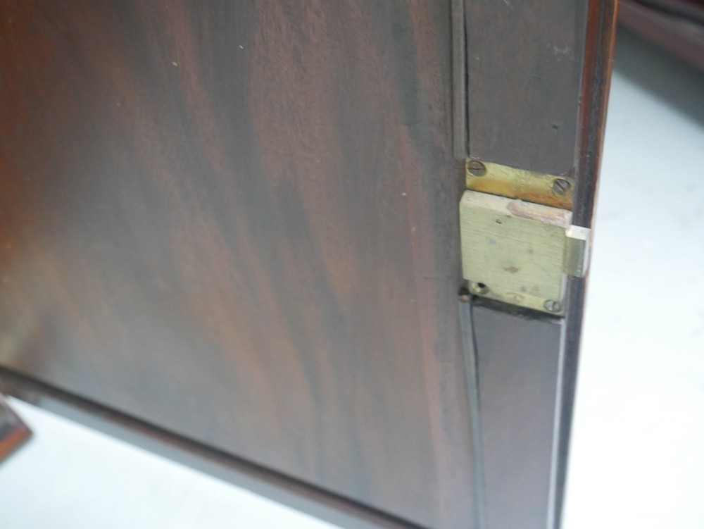 A low Georgian mahogany linen cupboard featuring two shaped panel doors, brass keyhole escutcheons, side handles, and bracket feet. View X