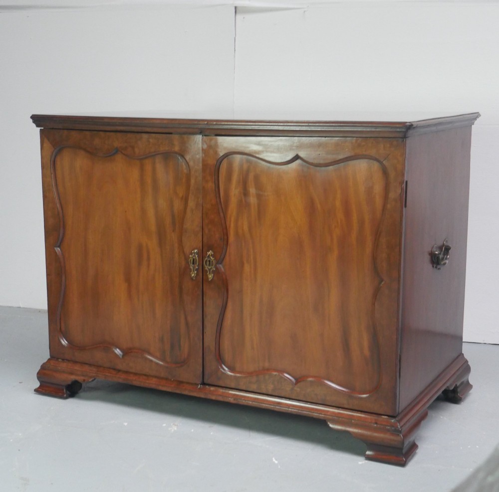 A low Georgian mahogany linen cupboard featuring two shaped panel doors, brass keyhole escutcheons, side handles, and bracket feet. View XI
