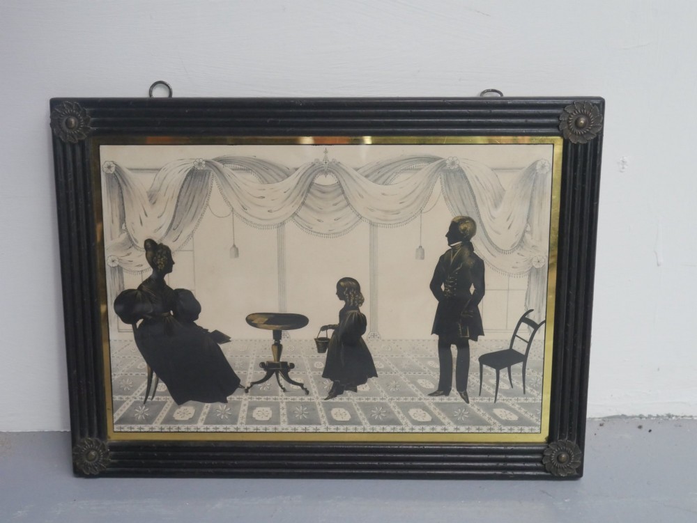 A framed antique Regency silhouette depicting a family group in a decorative interior setting set within an ebonised moulded frame with brass slip.
