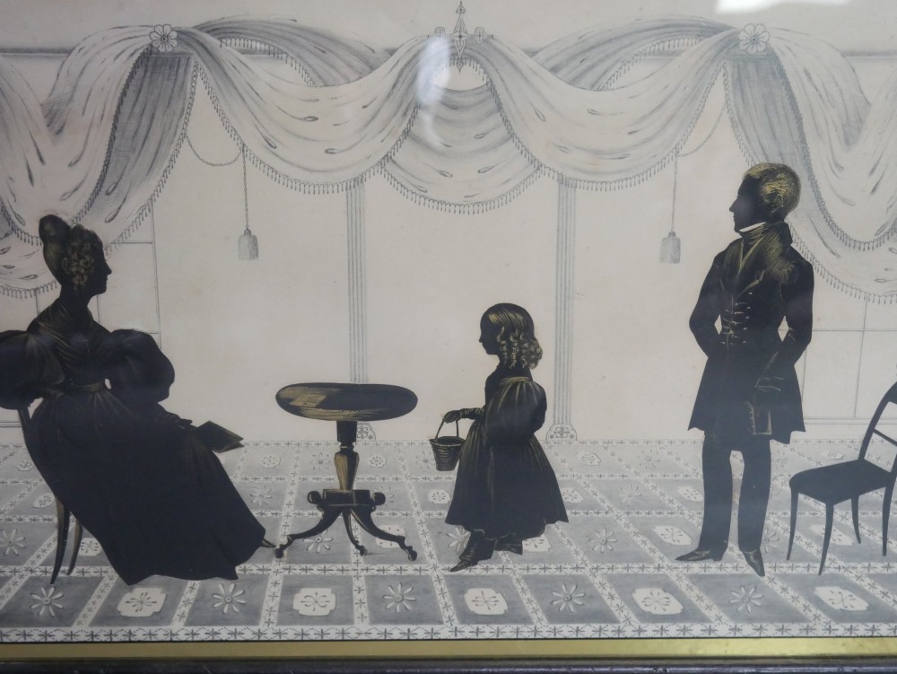 A framed antique Regency silhouette depicting a family group in a decorative interior setting set within an ebonised moulded frame with brass slip. View II