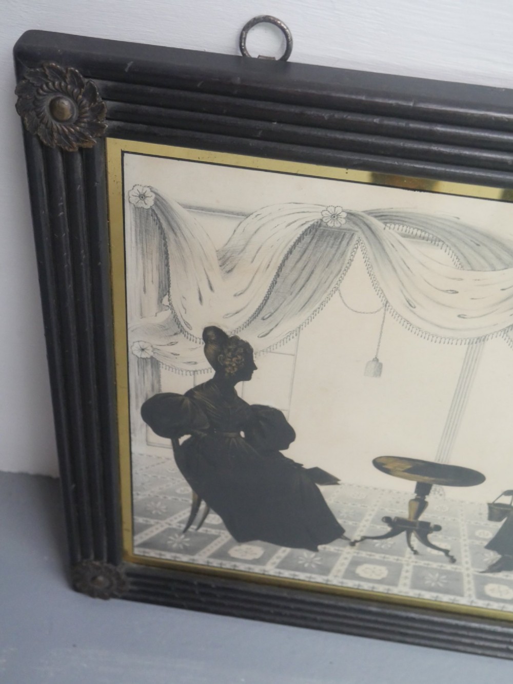 A framed antique Regency silhouette depicting a family group in a decorative interior setting set within an ebonised moulded frame with brass slip. View V