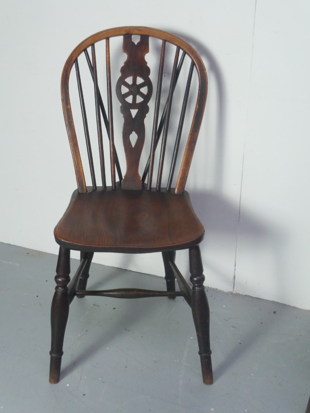 A set of four 19th-century dark wooden Windsor dining chairs featuring pierced wheelback central splats and turned legs. View V