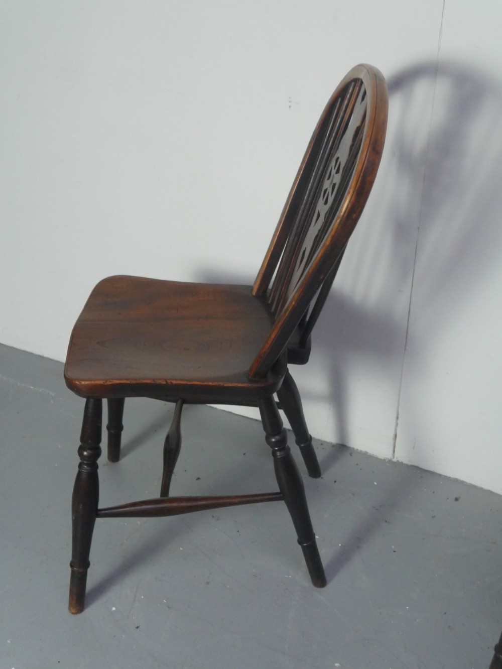 A set of four 19th-century dark wooden Windsor dining chairs featuring pierced wheelback central splats and turned legs. View VI