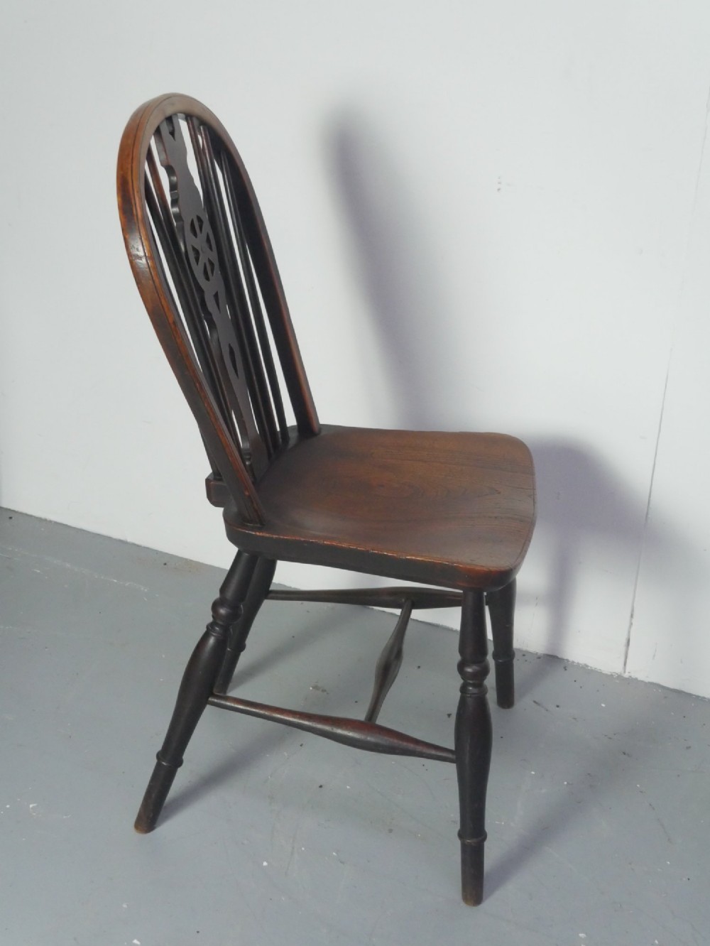 A set of four 19th-century dark wooden Windsor dining chairs featuring pierced wheelback central splats and turned legs. View VII