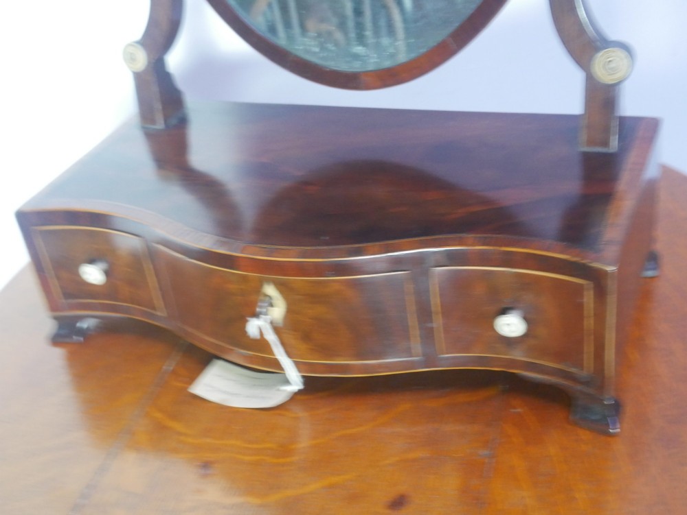 An antique Georgian mahogany dressing mirror with an oval adjustable glass supported on curved arms above a serpentine three-drawer base. View II