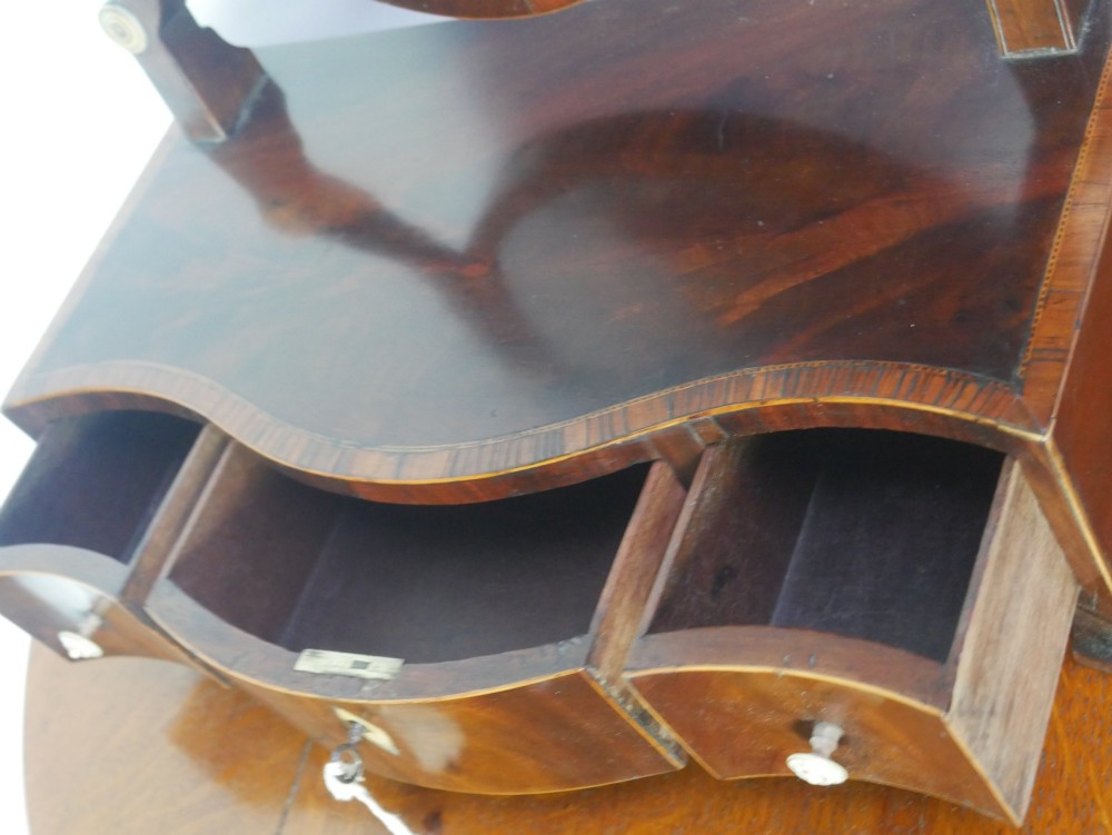 An antique Georgian mahogany dressing mirror with an oval adjustable glass supported on curved arms above a serpentine three-drawer base. View VII