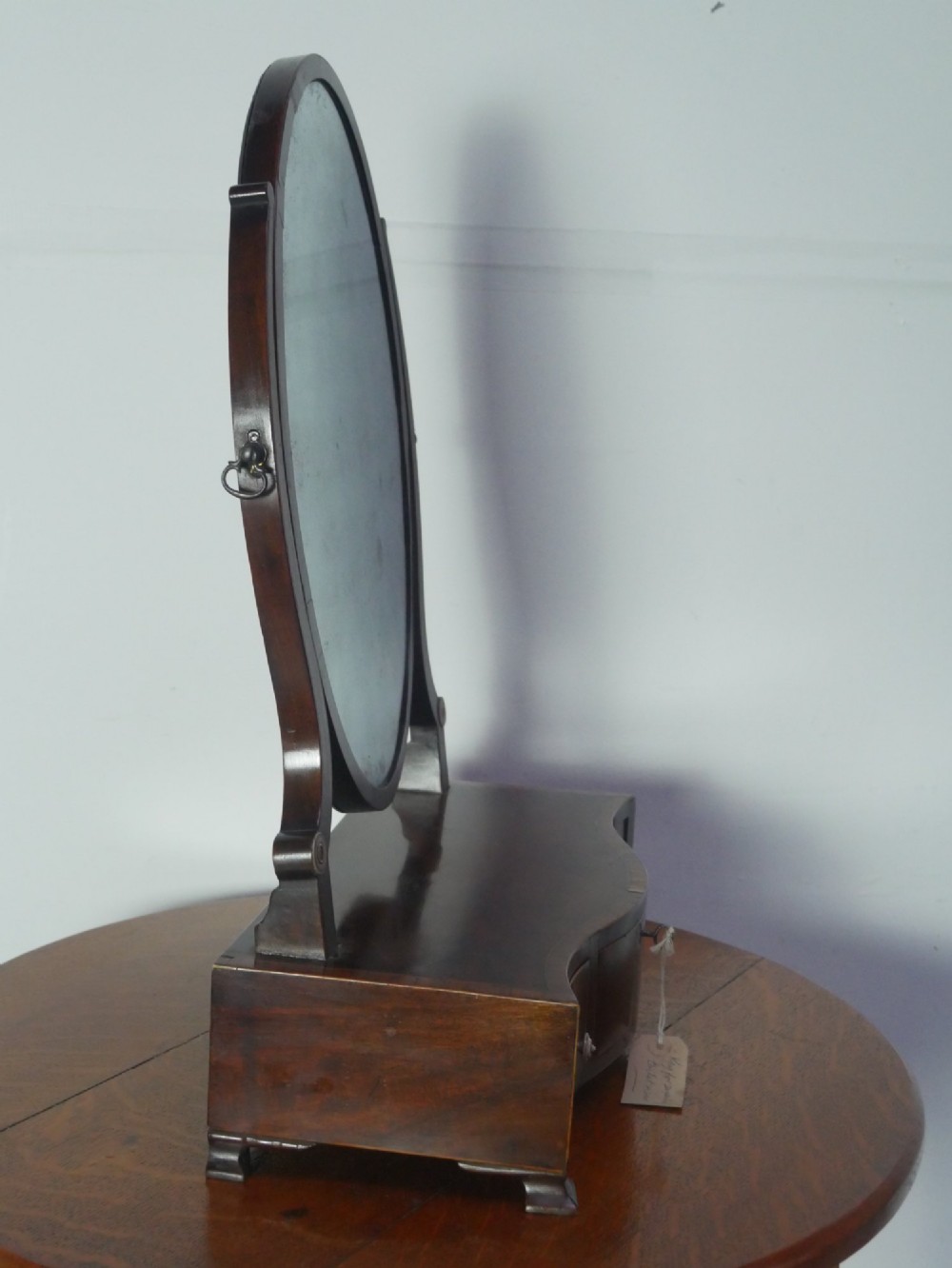 An antique Georgian mahogany dressing mirror with an oval adjustable glass supported on curved arms above a serpentine three-drawer base. View IX